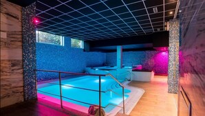 Ein moderner Poolbereich im Innenbereich mit blauer Mosaikwand, einer klaren Glasscheibe und Holzboden.
