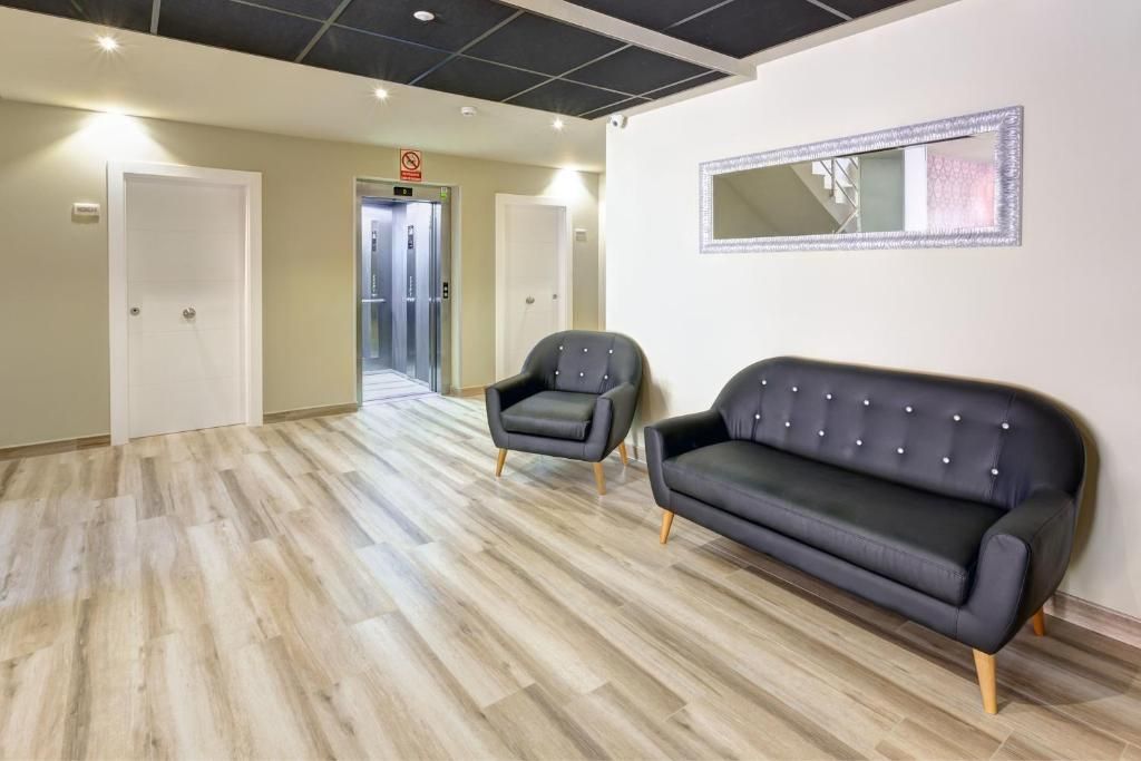 A hallway with a black leather sofa and a chair, a mirror on the wall, and an elevator in the background.