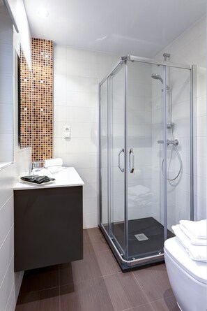 Un baño moderno con ducha acristalada, lavamanos blanco y salpicadero de azulejos.