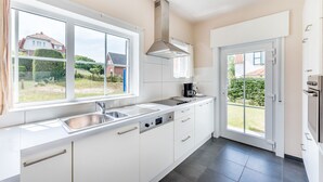 Et moderne køkken med hvide skabe, en stålvask og et stort vindue med udsigt til et boligområde.