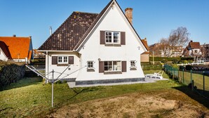 Et hvidt hus med brune skodder, skråtag og en synlig skorsten.