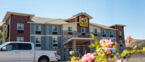 A multi-story hotel with a 'My Place' sign, a parking lot, and a clear sky.