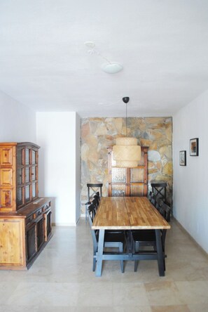 A dining area with a wooden table and chairs, a stone wall, and a hanging light fixture. - Villa Casa Blanca (Costa Adeje)