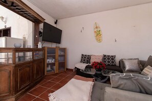 A living room with a wooden cabinet, a television, a surfboard decoration, and a sofa with patterned cushions. - Villa Casa Blanca (Costa Adeje)