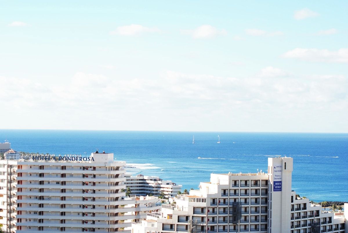 A coastal hotel with multiple floors, balconies, and a view of the sea.
