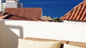 A balcony with a view of the ocean, a wicker sofa with cushions, and a tiled roof. - Villa Casa Blanca (Costa Adeje)
