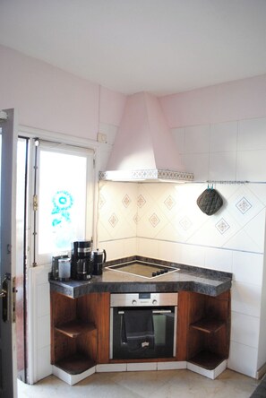 A compact kitchen with a built-in oven, a coffee maker, and a hanging pot rack. - Villa Casa Blanca (Costa Adeje)