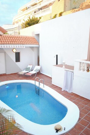 A swimming pool with a ladder, two lounge chairs, and a small table with a lamp. - Villa Casa Blanca (Costa Adeje)