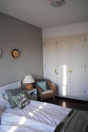 A bedroom with a bed, a nightstand, a chair, a wardrobe, and a ceiling light. - Villa Casa Blanca (Costa Adeje)