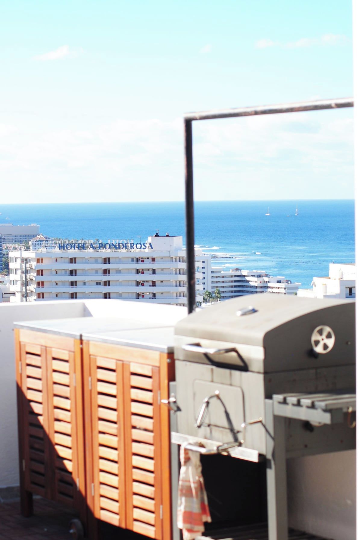 A rooftop terrace with a view of the sea and Hotel A Ponderosa in the background.