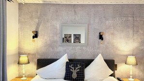 Une chambre avec un mur en béton, un tableau encadré, deux lampes de chevet et un coussin en forme de cerf.