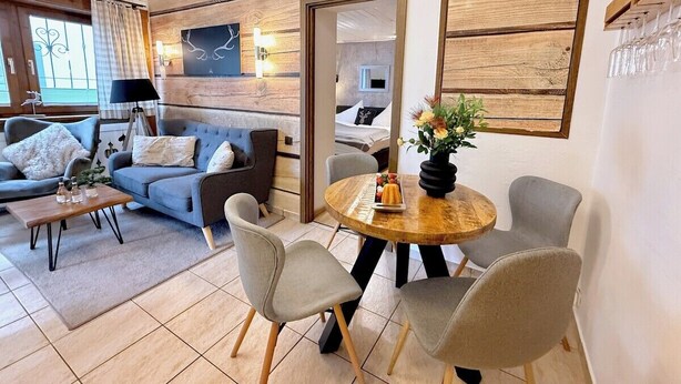 Un salon moderne avec un canapé, des fauteuils, une table basse et une table à manger agrémentée d’un vase de fleurs.