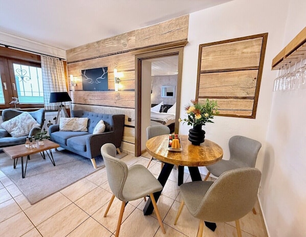 A modern living room with a sofa, chairs, a coffee table, and a dining table with a vase of flowers.