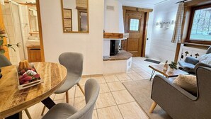 Une pièce comprenant une table à manger en bois, des chaises grises, un canapé, une cheminée et une fenêtre avec des rideaux.