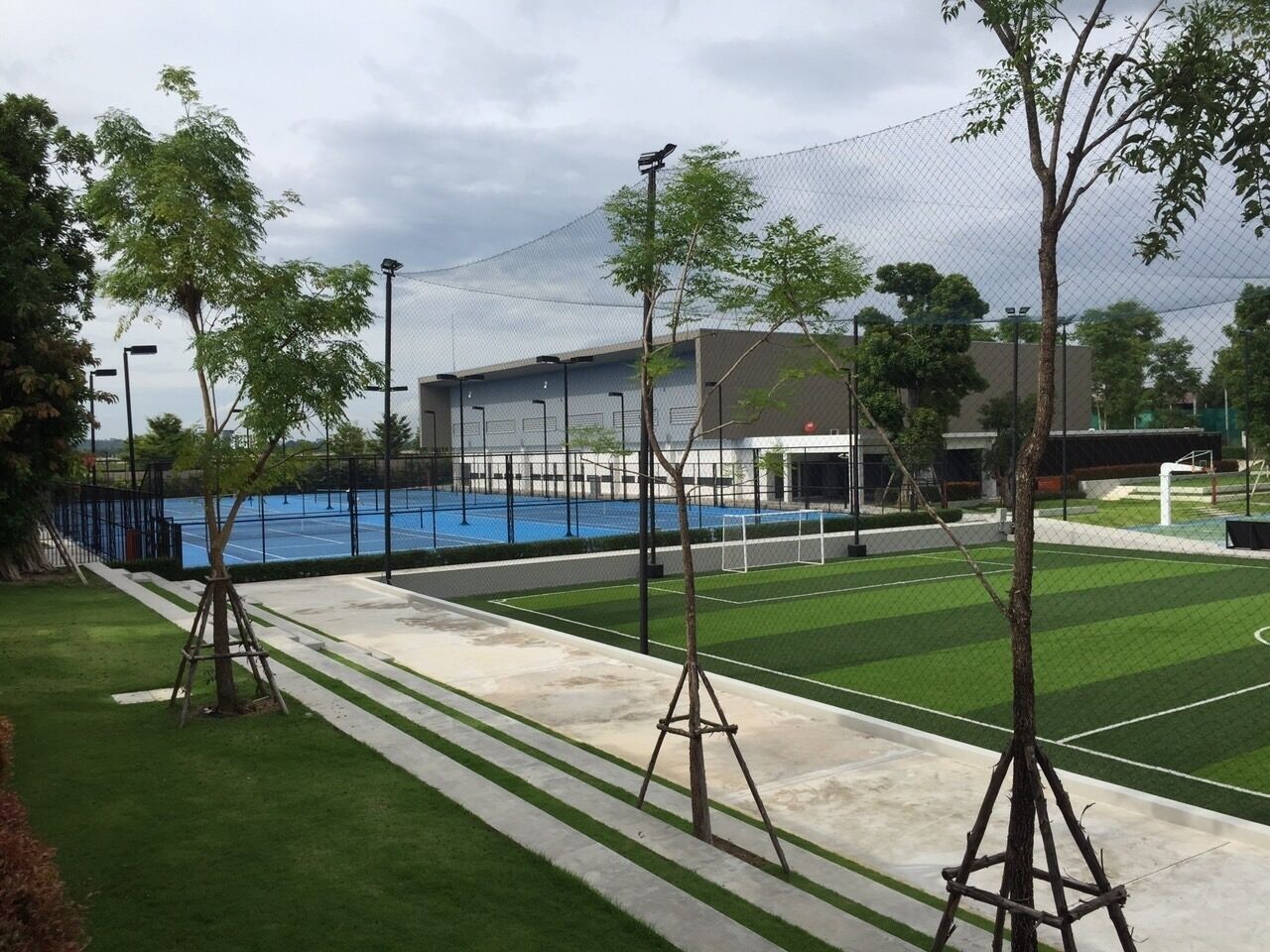 A sports facility with a tennis court, a basketball court, and a fenced area.