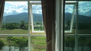 Une pièce dotée d’une grande fenêtre donnant sur un paysage verdoyant et des montagnes.