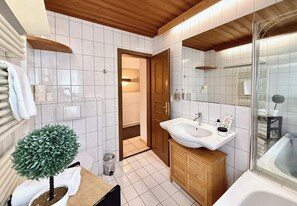 Une salle de bain avec des carreaux blancs, un plafond en bois, un lavabo, un miroir et une douche.