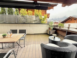 A wooden deck with a table and chairs, surrounded by wicker furniture and potted plants. - Cozy design apartment in the heart of Kitzbühel (Kitzbühel)