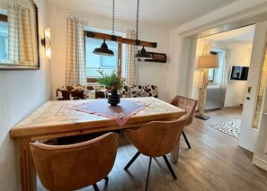 Un coin repas comprenant une table en bois, quatre chaises, un vase avec une plante et un chemin de table Ă carreaux.