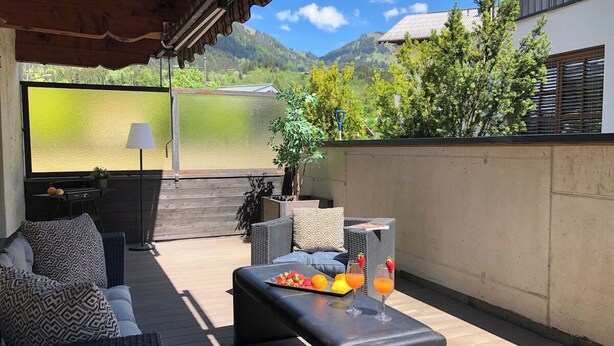 A covered outdoor seating area with a table, cushions, and a tray of fruit and drinks. - Belle Kitz 2 by Belle-Stay (Kitzbühel)