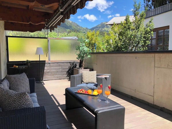 A covered outdoor seating area with a table, cushions, and a tray of fruit and drinks. - Cozy design apartment in the heart of Kitzbühel (Kitzbühel)