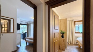 A hotel room with a wooden floor, a bed, a bedside table with a plant, and a window with curtains. - Belle Kitz 2 by Belle-Stay (Kitzbühel)