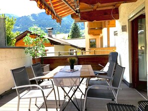 Une table en bois avec des chaises sur un balcon, une plante en pot et une vue sur les montagnes.