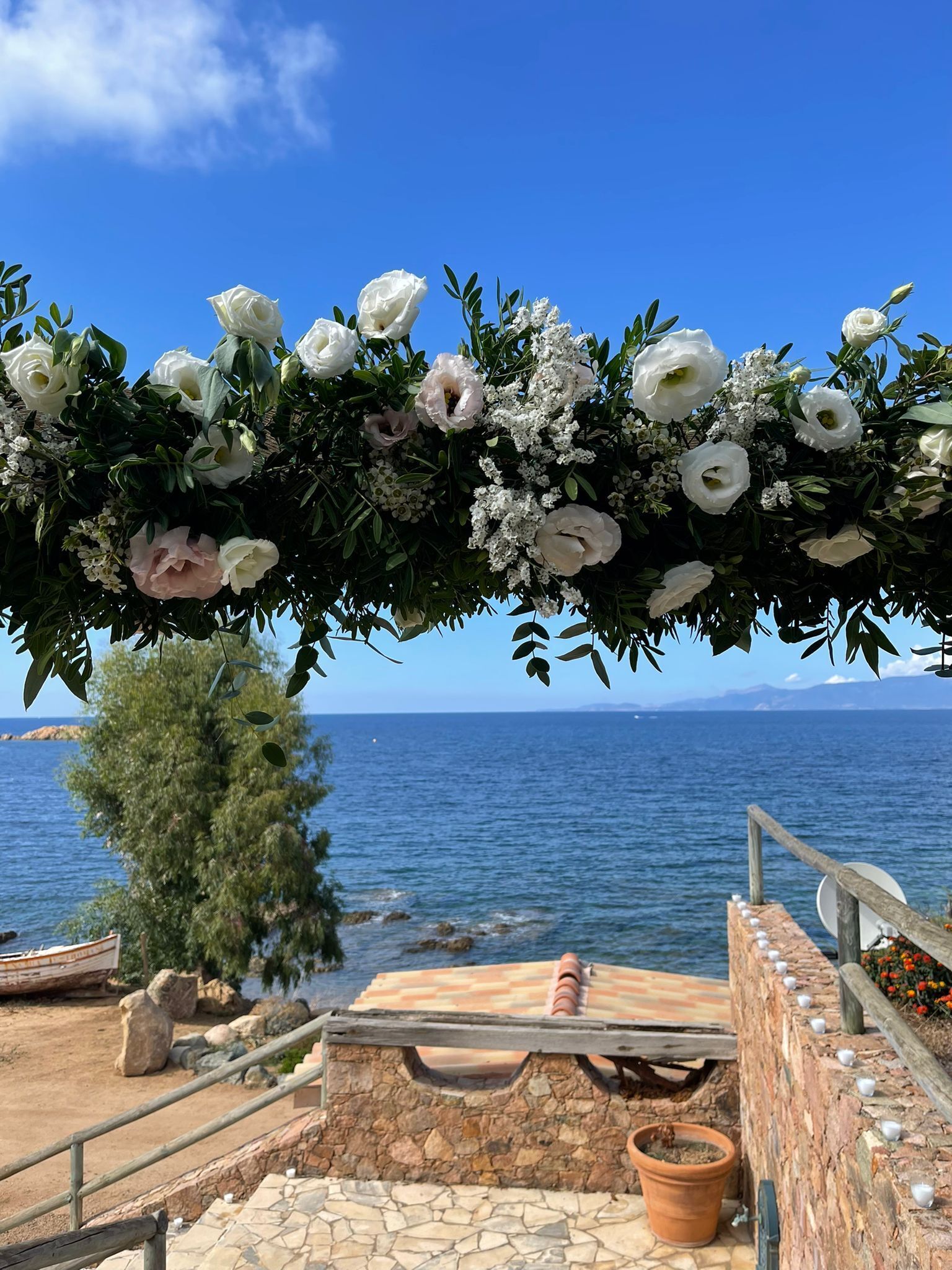 Een uitzicht op de kust, met een stenen pad dat leidt naar een zitgedeelte onder een bloemrijke boog.