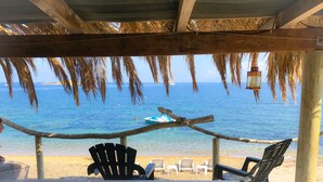 Une vue sur la plage avec une structure en bois au-dessus, une eau d’un bleu limpide et plusieurs chaises de plage.
