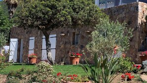 Un bâtiment en pierre avec un jardin à l’avant, agrémenté de plantes en pot et de rochers.
