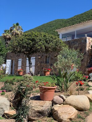A stone building with a garden in front, featuring potted plants and rocks.