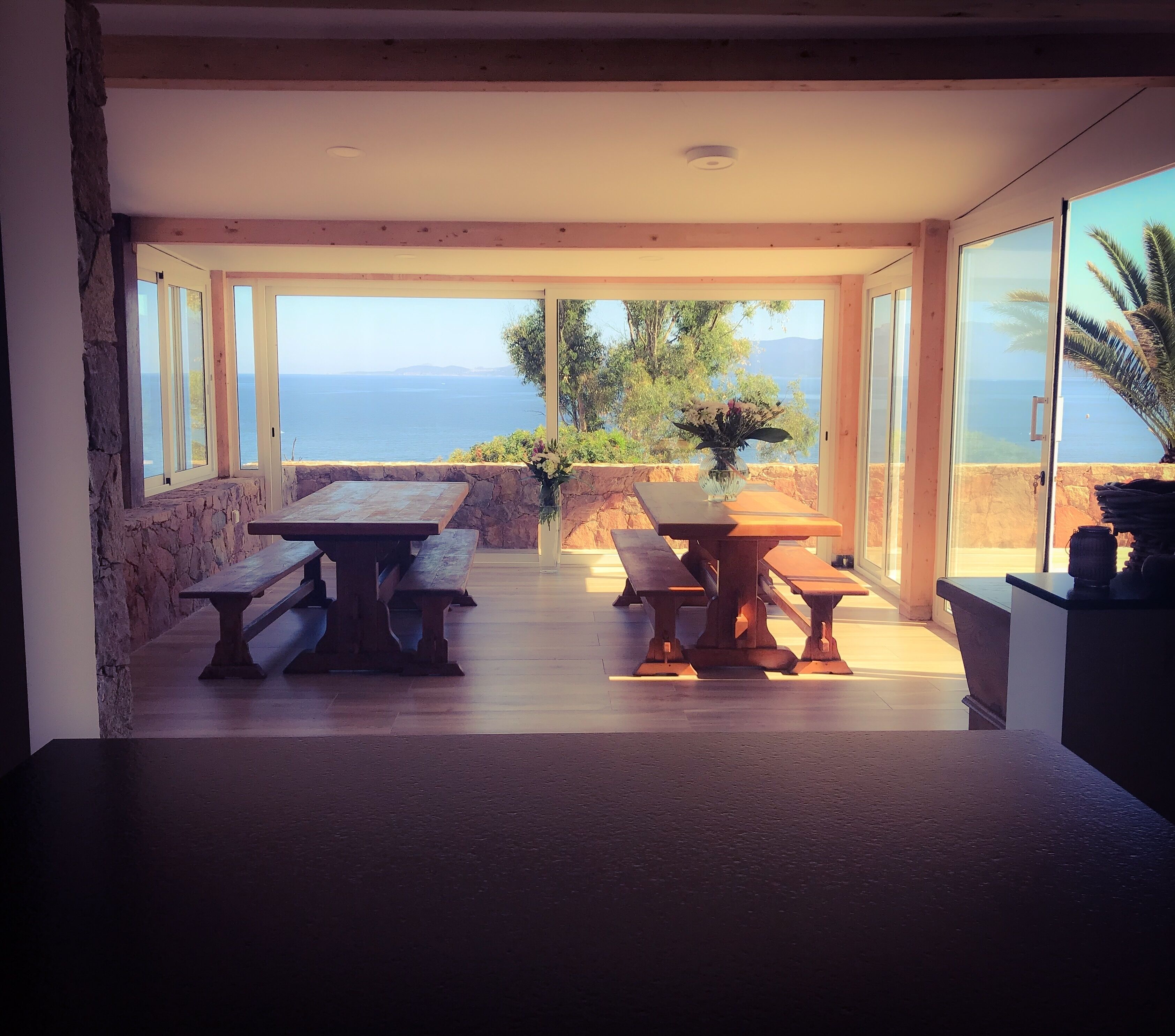 A modern dining area with a stone wall, wooden benches, and a table with a vase of flowers.