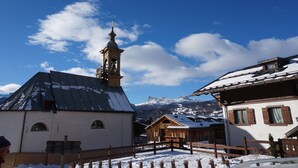 A traditional wooden building with a bell tower, surrounded by snow-covered roofs and mountains in the background. - Casa Alverà (Cortina d´Ampezzo)