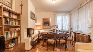 A cozy living room with a wooden bookshelf, a fireplace, a dining table with chairs, and a comfortable sofa. - Casa Alverà (Cortina d´Ampezzo)