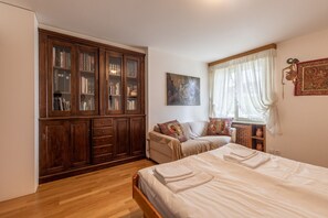 A bedroom with a large wooden wardrobe, a bed with neatly folded towels, a window with sheer curtains, and a wall-mounted artwork. - Casa Alverà (Cortina d´Ampezzo)