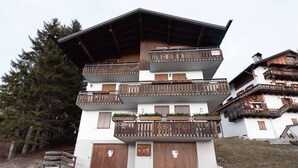 A multi-story building with wooden balconies, a sloped roof, and a sign indicating a ski resort. - Casa Alverà (Cortina d´Ampezzo)