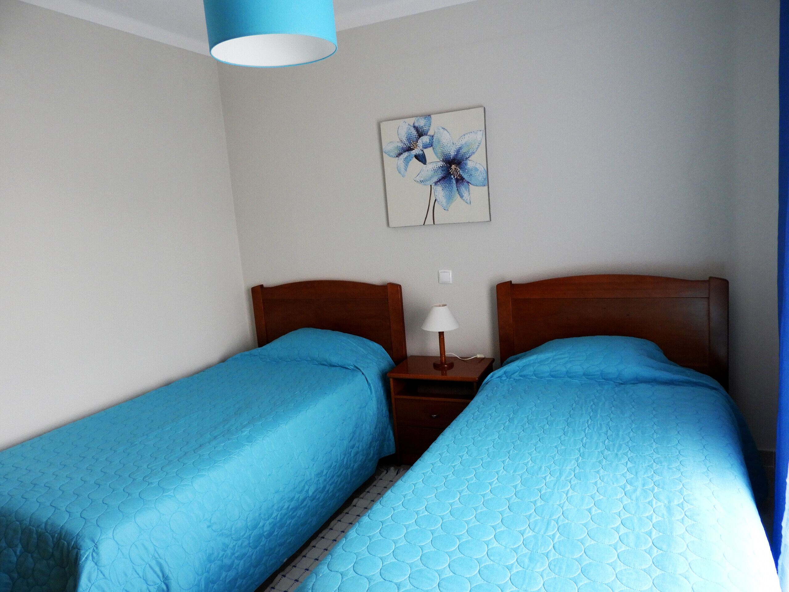 A hotel room with two single beds, a nightstand with a lamp, and a painting on the wall.