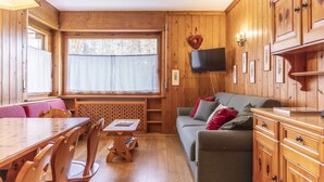 Un intérieur en bois comprenant une table à manger, des chaises, un canapé et un téléviseur fixé au mur.