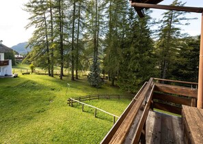 Un pontile in legno con vista su una zona erbosa, alberi e un edificio in lontananza.