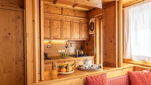 A cozy cabin-style kitchen with wooden cabinets, a stove, and a breakfast bar with seating. - Casa Pecol (Cortina d´Ampezzo)