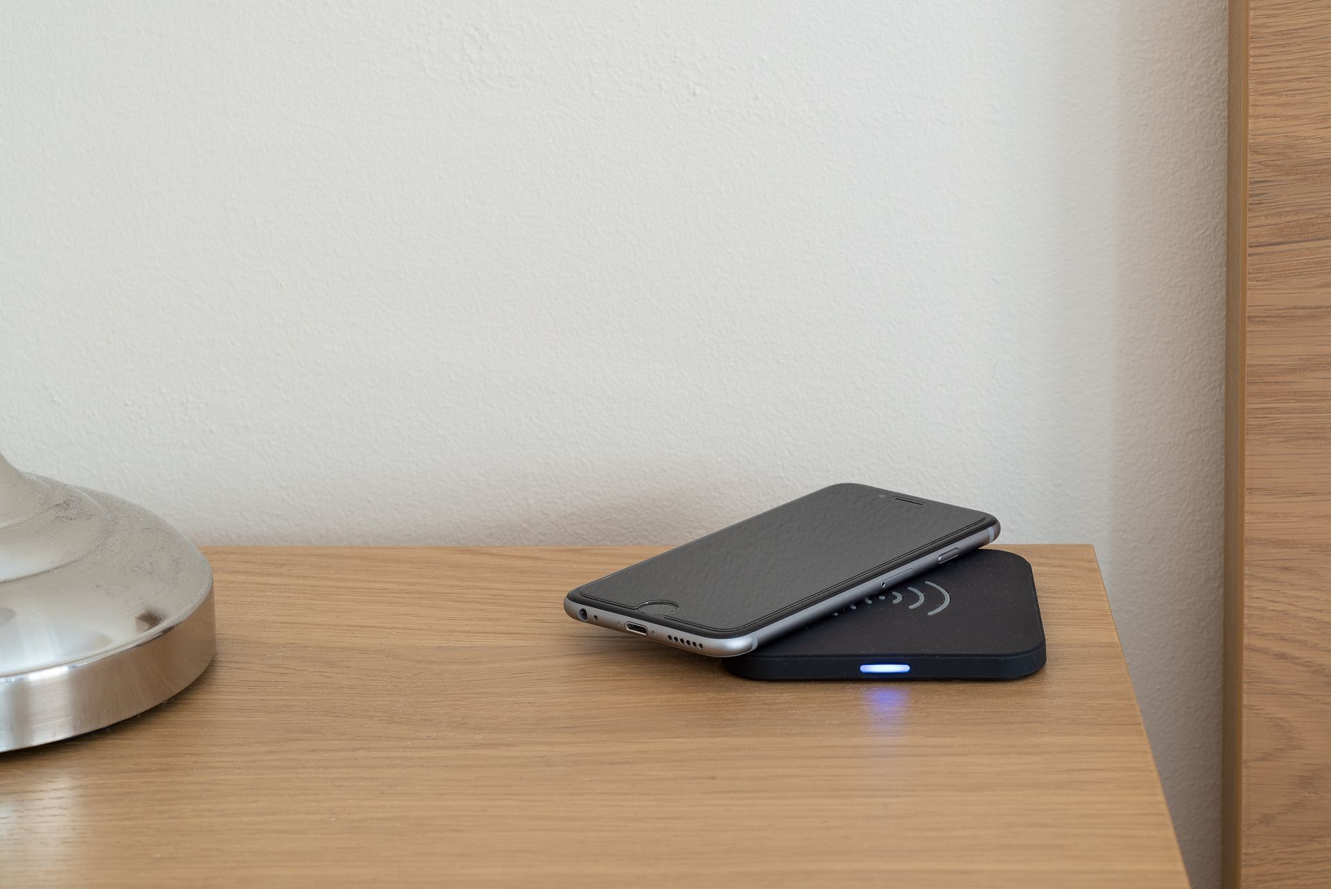 A smartphone on a charging dock with a metal base and a wooden surface.