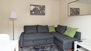 Moderni olohuone, jossa on harmaa kulmasohva, valkoinen sivupöytä, lattiavalaisin ja kaksi maailmankarttaa seinillä.