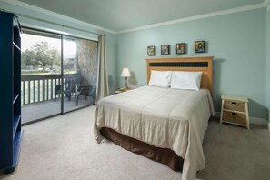 Quarto com cama, mesa de cabeceira, abajur, mesa pequena e vista para o exterior.