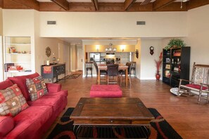 A spacious living room with a red sofa, a wooden coffee table, and a dining area with chairs and a kitchen in the background.