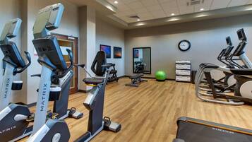 Un gimnasio con diferentes máquinas de cardio, una cinta de correr y un espejo grande.