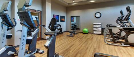 A gym with various cardio machines, a treadmill, and a mirrored wall.