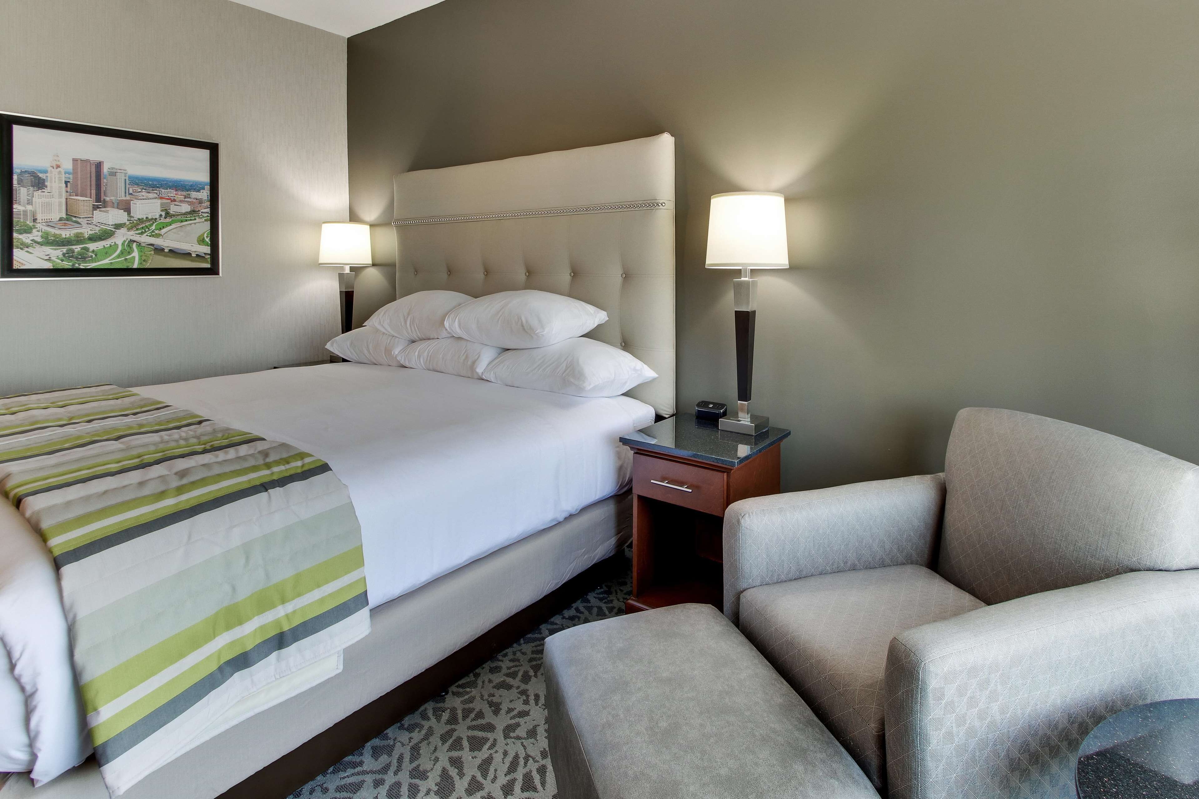 A hotel room with a bed, a chair, a nightstand, and a lamp.