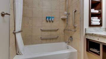 Ein Badezimmer mit einer Badewanne, Haltegriffen, einem Handtuchhalter und einem Ablagebereich mit Handtüchern.
