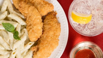 A plate of breaded chicken cutlets with pasta and a glass of iced drink with a lemon slice.