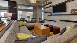 A modern living room with a sectional sofa, a wooden coffee table, and a flat-screen TV mounted on a brick wall. - Drury Inn & Suites Columbus Polaris (Columbus)